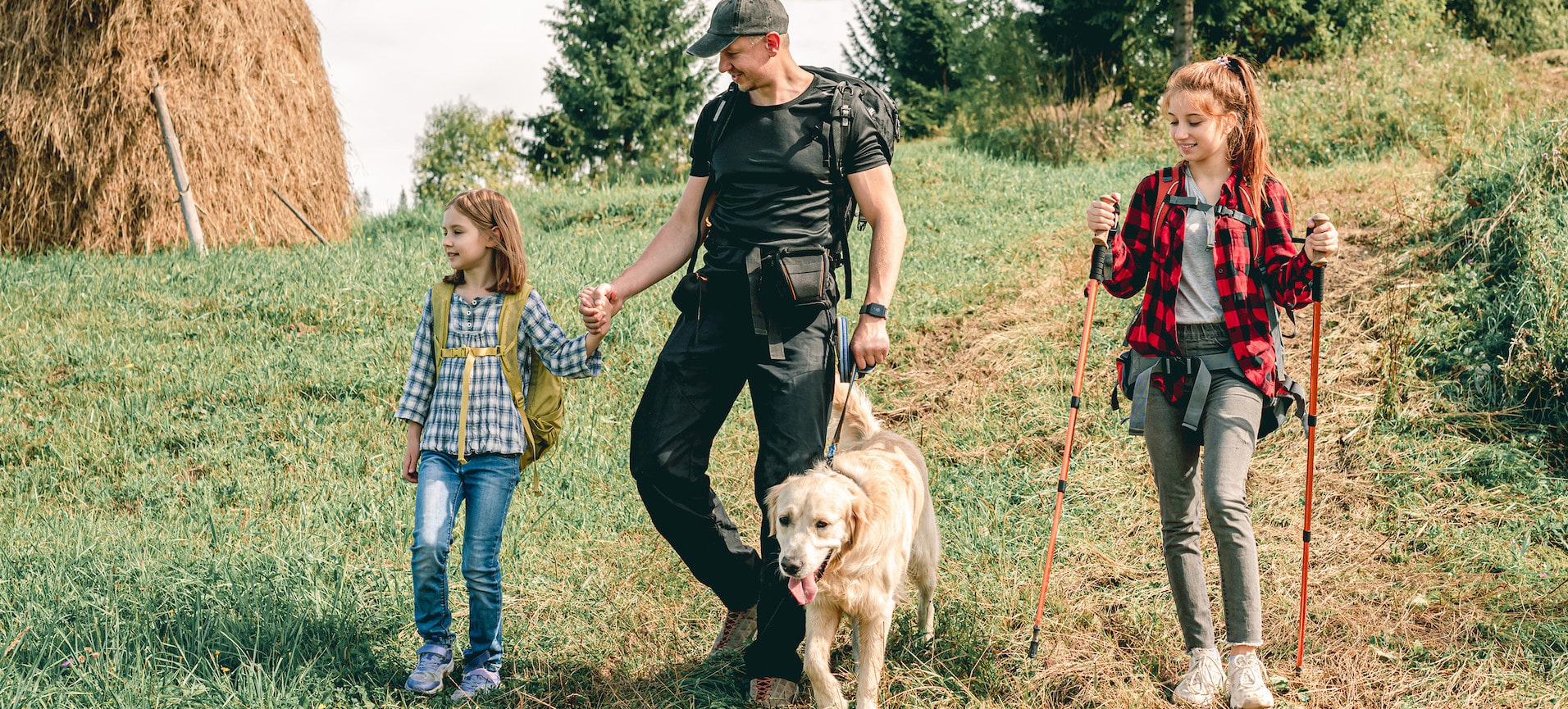 Familie wandert mit Hund über eine Wiese in Südtirol – Vater und zwei Kinder genießen gemeinsam die Zeit in der Natur.