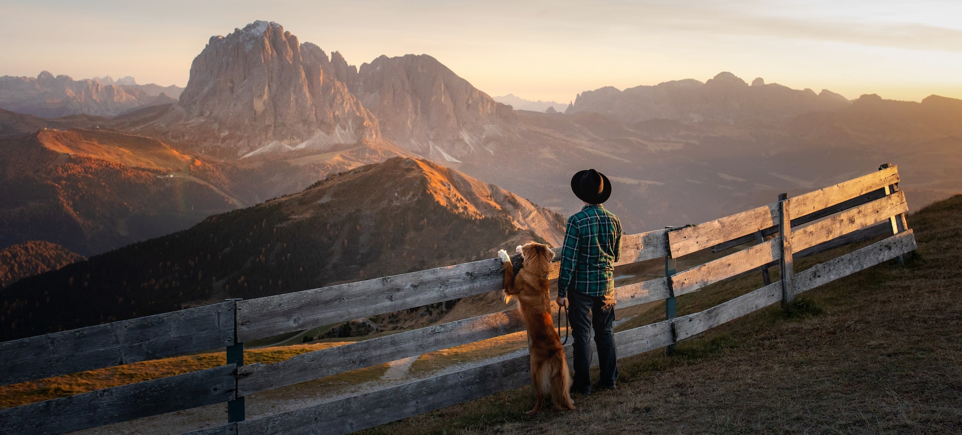 Person mit Hund blickt über die Berge Südtirols bei Sonnenuntergang – ein Moment von Ruhe, Freiheit und Verbundenheit in der Natur.