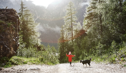 Kind läuft mit Hund auf einem Waldweg im Pustertal – Sonnenlicht fällt durch die Bäume, frische Bergluft in Südtirol.