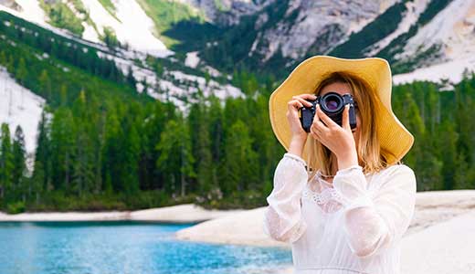 Fotospot und Fotografie am Pragser Wildsee Urlauberin hält eine Kamera vor das Gesicht am Pragser Wildsee mit Sicht auf Nadelwälder und Felswände