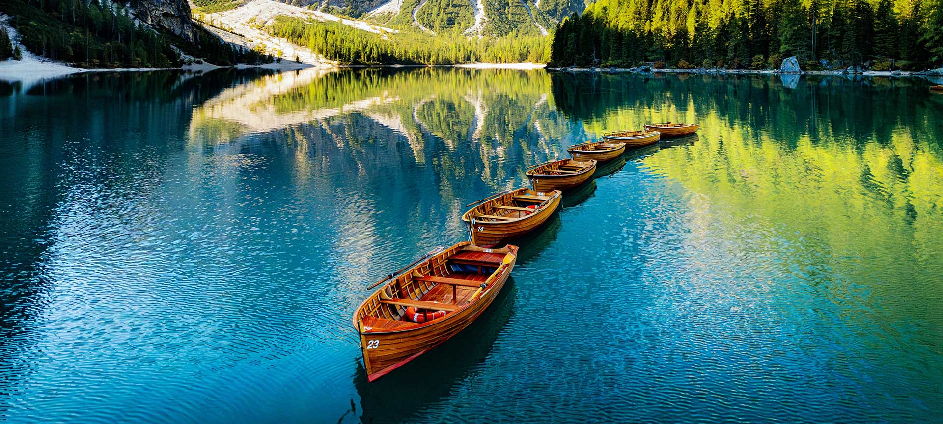Aufgereihte Holzruderboote auf dem Pragser Wildsee Geschwungene Kette historischer Holzruderboote im leuchtend türkisfarbenen Wasser des Pragser Wildsees